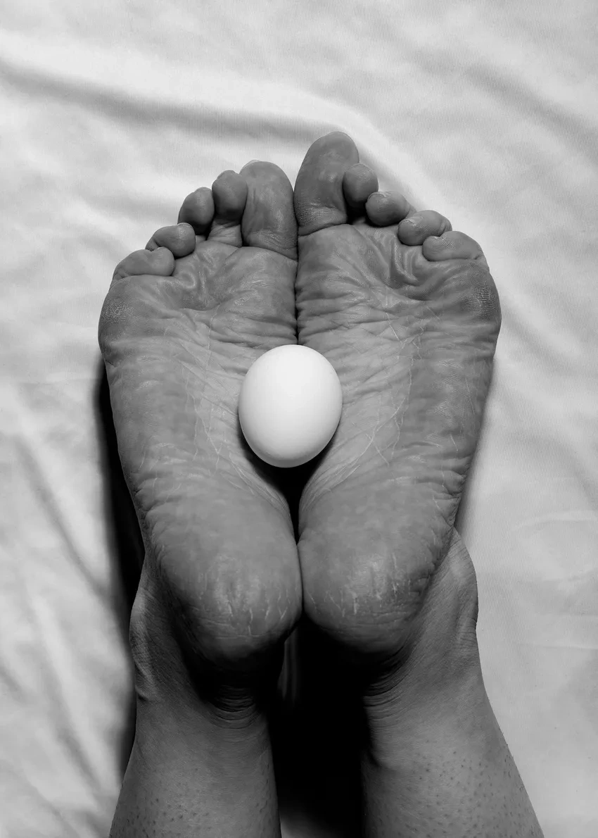Feet holding an egg on white sheet