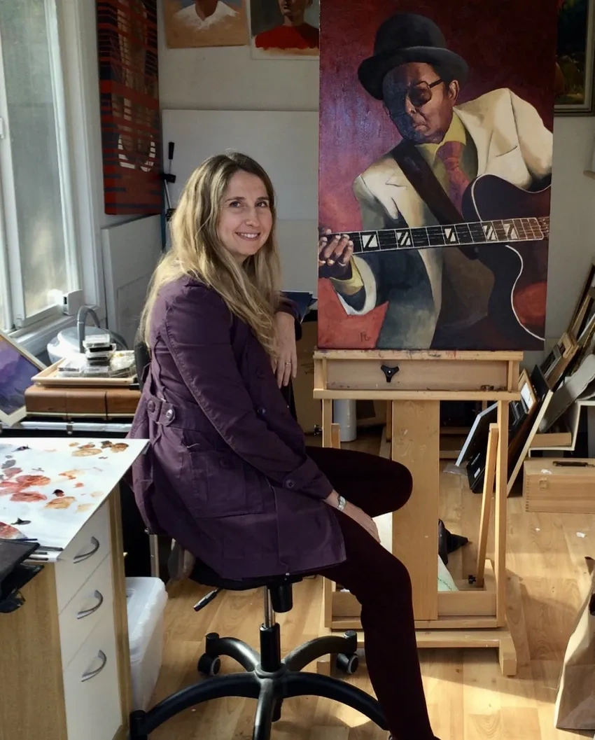 Artist sitting beside her guitar painting