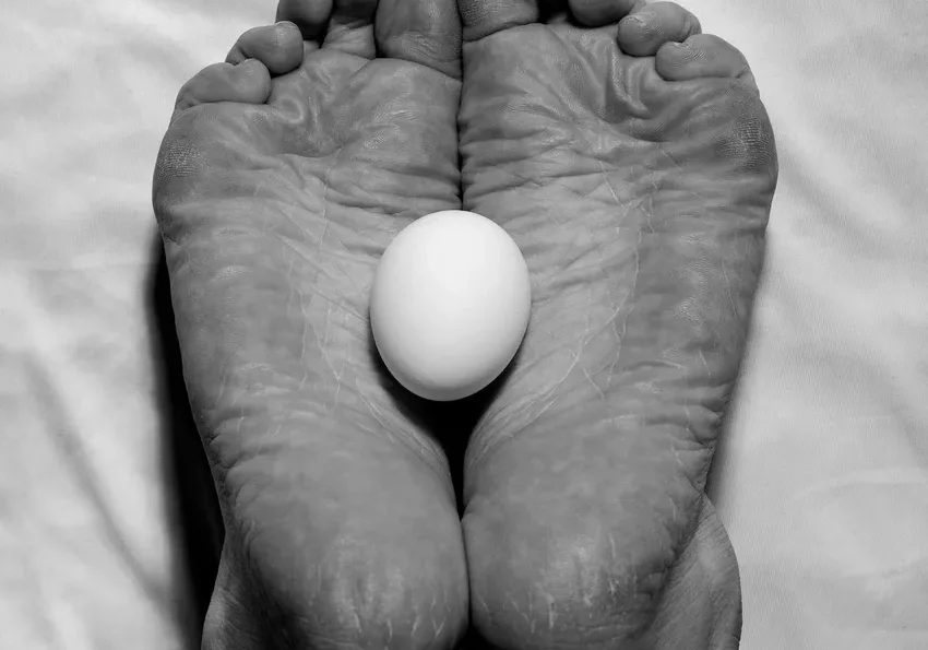 Feet holding an egg on white sheet