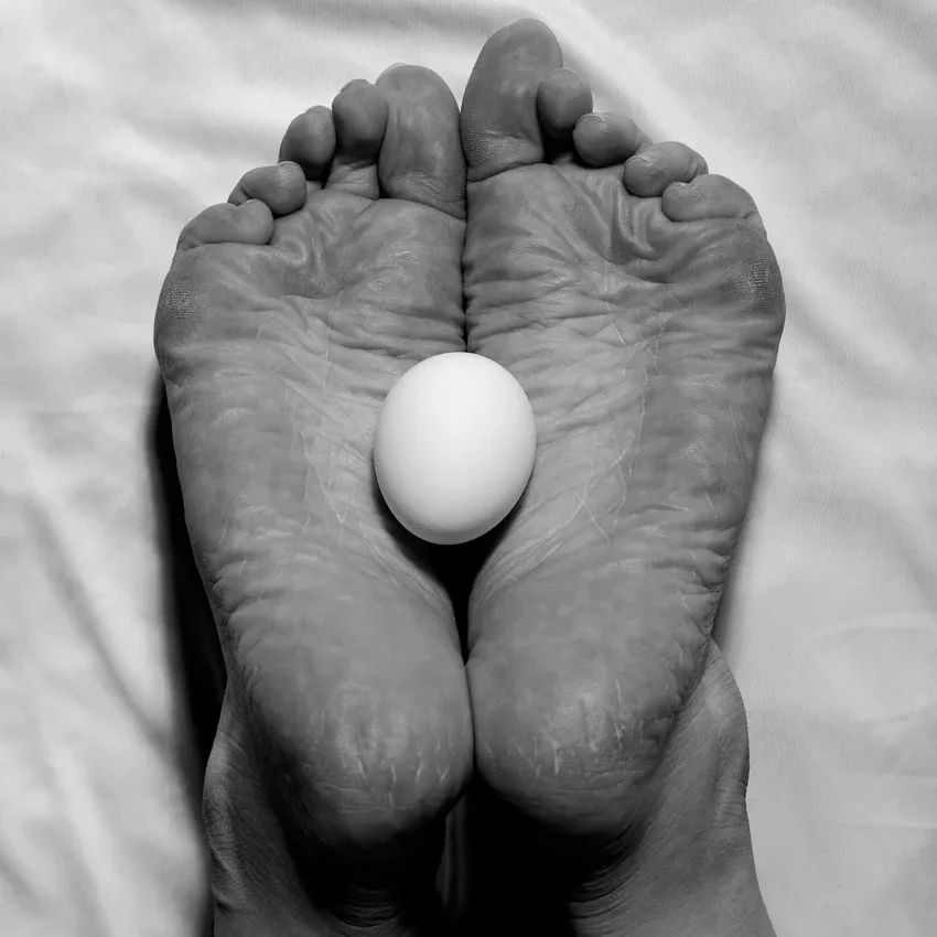 Feet holding an egg on white sheet