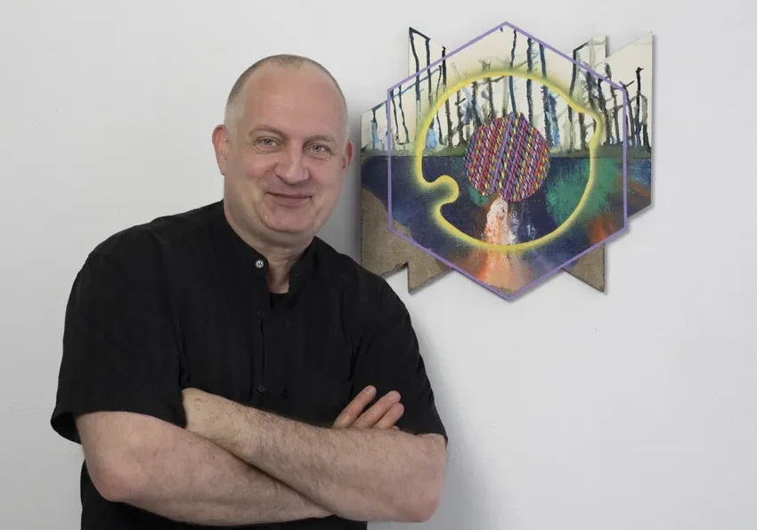 Smiling man with folded arms near artwork
