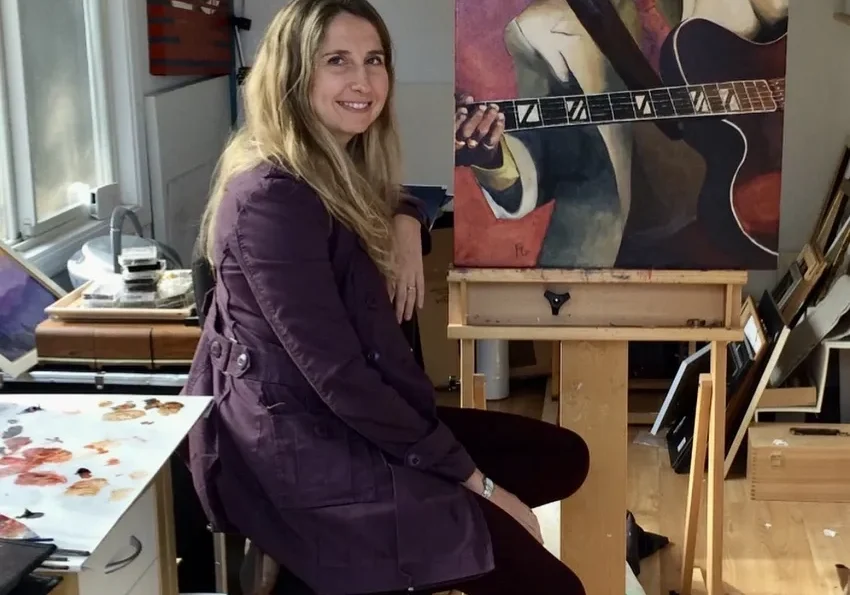 Artist sitting beside her guitar painting