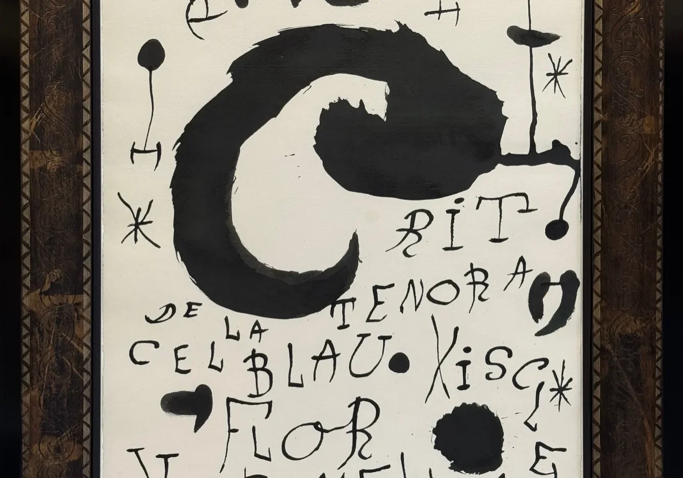 Framed view of Joan Miró’s For Les Essencies de la Terra (1968), with a sweeping black ink curve, handwritten letters and star-like marks on pale paper